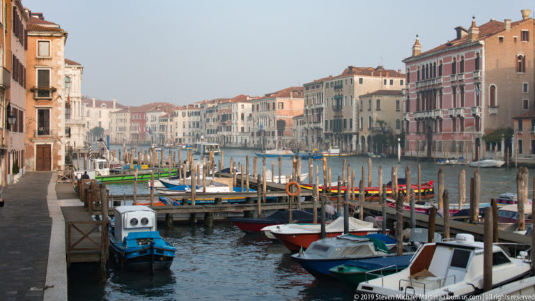 Small boats and floating docks beside the Grand Canal, with rows of historic palazzi receding into the distance.