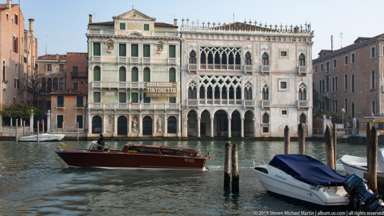 Ca' d'Oro's ornate Venetian Gothic façade across the Grand Canal, with a motorboat and mooring posts in front.