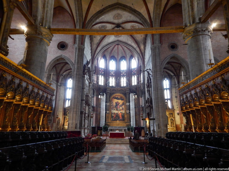 Central aisle between dark choir stalls and gilded canopies leading through tall Gothic arches toward the distant high altar.