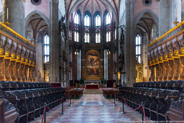 Long central aisle between dark carved choir stalls leading toward the high altar and bright Gothic apse windows.