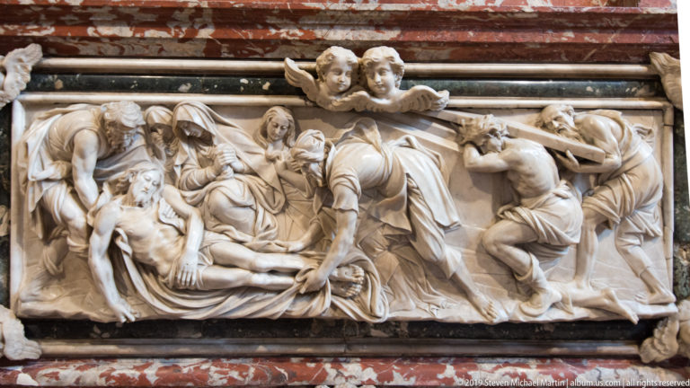 White marble relief of the dead Christ surrounded by mourning figures, with clustered bodies and expressive gestures in high relief.