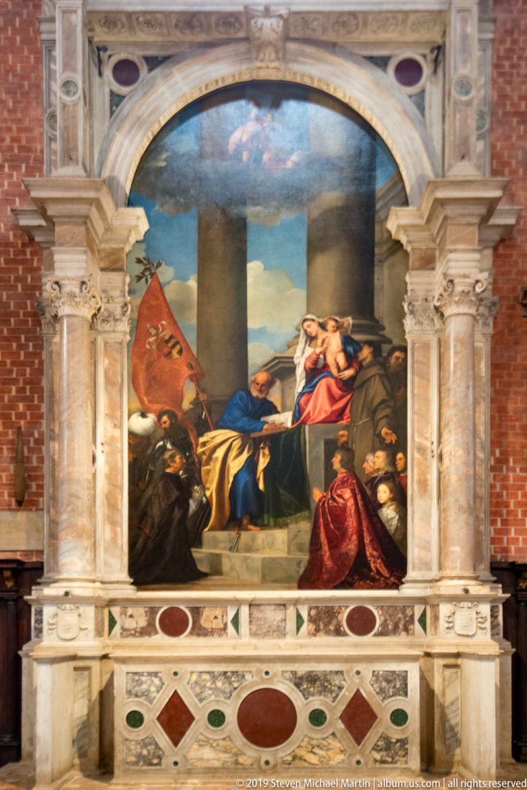 Large religious painting in a marble frame, with a kneeling man at right, sacred figures at center, and a red Venetian banner at left.
