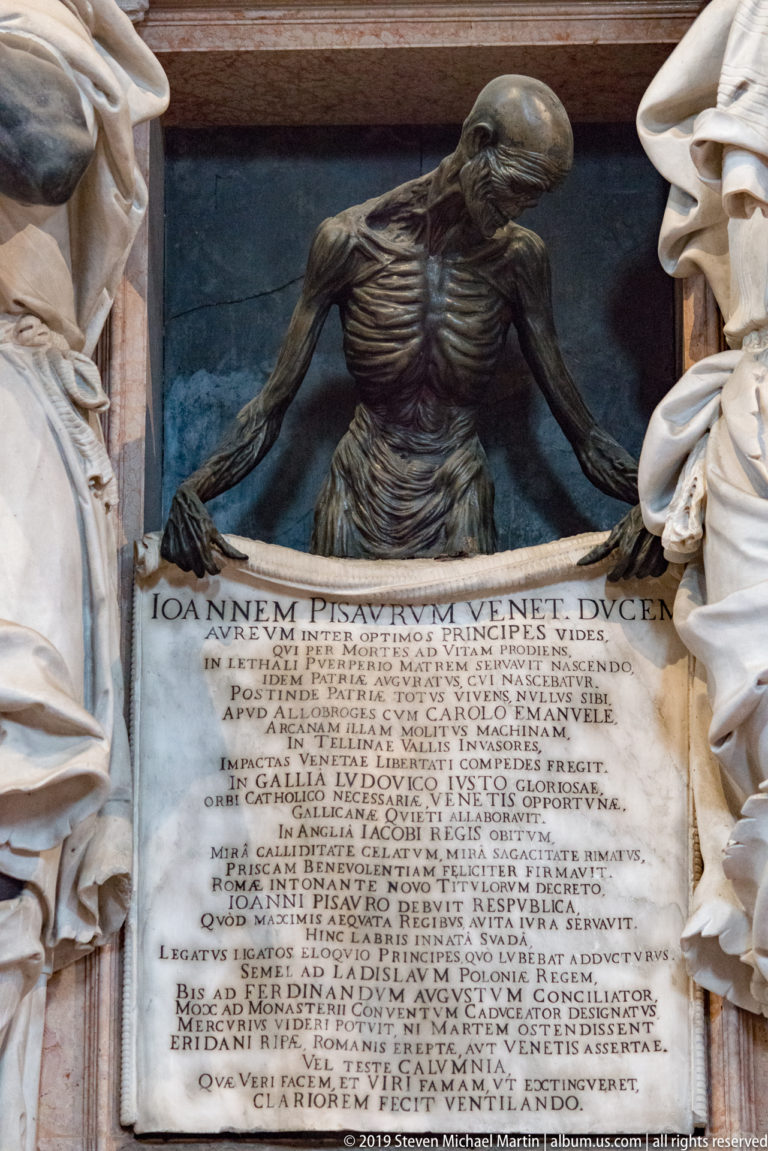 Dark skeletal figure with exposed ribs spreads its arms above an inscribed stone tablet, framed by pale draped sculptures.