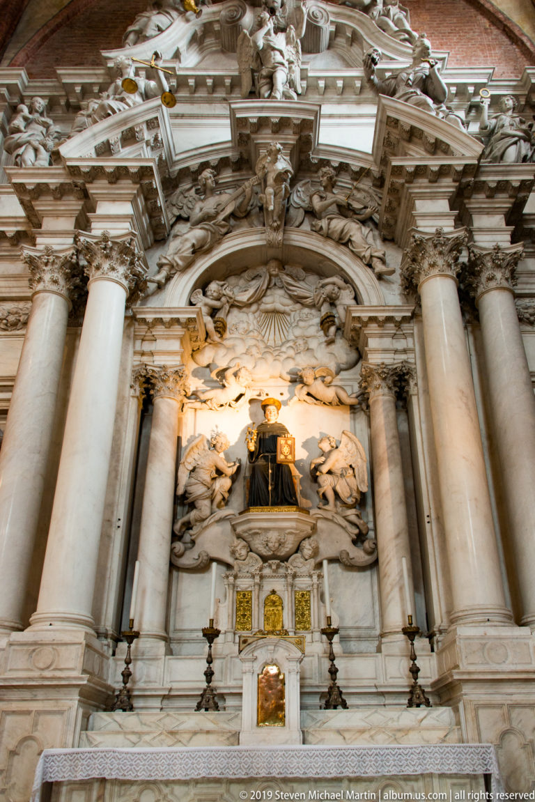 Large columned side altar with a dark-robed saint at center, surrounded by pale angels, clouds, and reclining figures above.