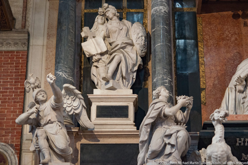 White marble funerary sculpture with an enthroned central figure above a pedestal, flanked by expressive angels against brick and dark columns.
