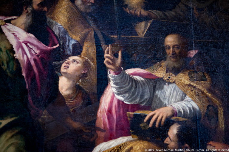 Detail of a religious painting with a bearded cleric in ornate vestments raising his hand beside a younger figure looking upward.