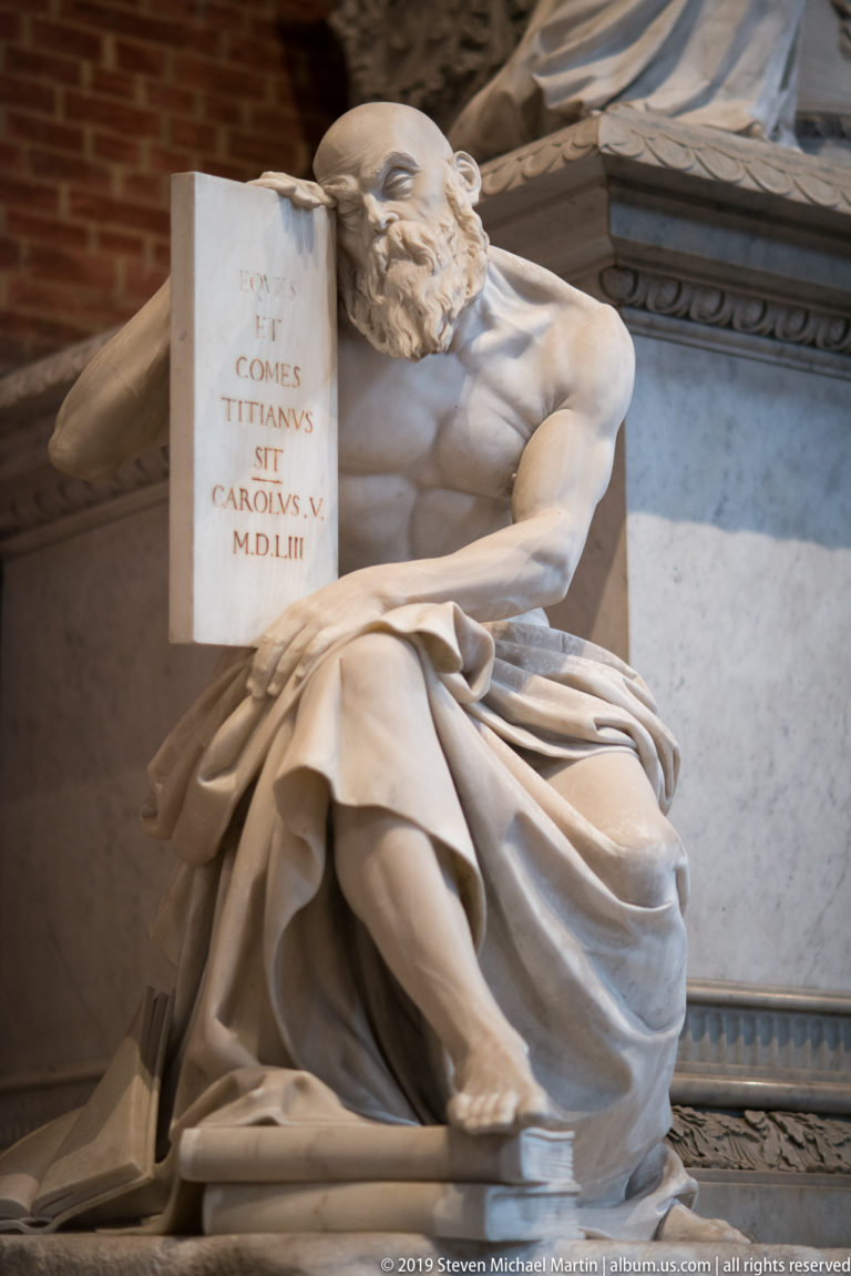 Seated marble figure in drapery holding an inscribed tablet with the Roman-numeral date MDLIII beside a funerary monument.