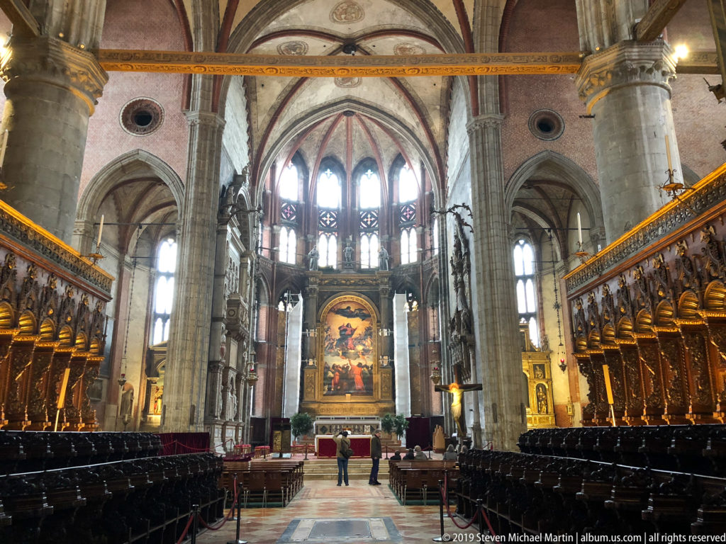 Central view between dark wooden choir stalls toward the high altar, framed by pointed arches, tall piers, and a large traceried window.