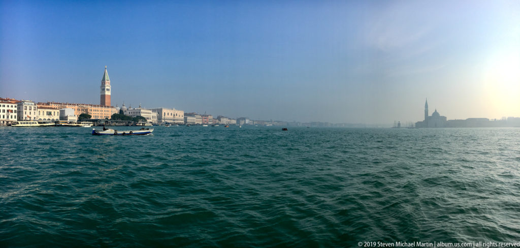 Wide lagoon view with St. Mark’s waterfront at left and hazy San Giorgio Maggiore silhouette at right.