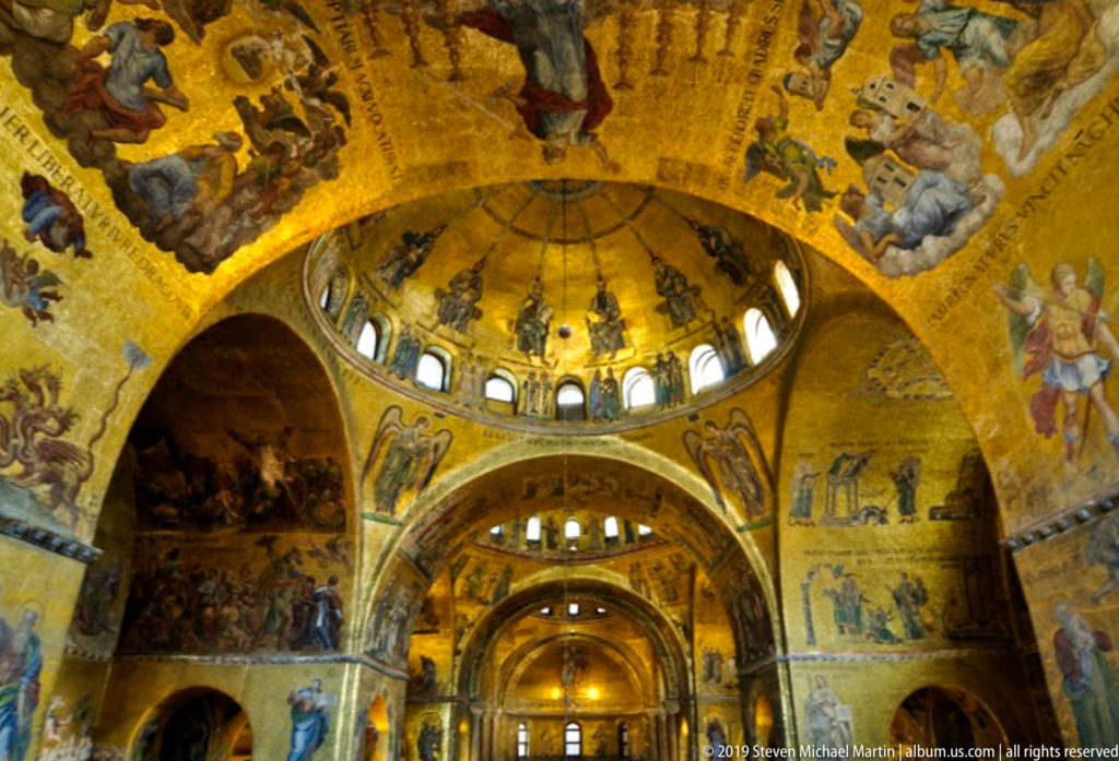 Golden mosaic-covered domes and arches inside St. Mark's Basilica, with small windows circling the central dome above the nave.