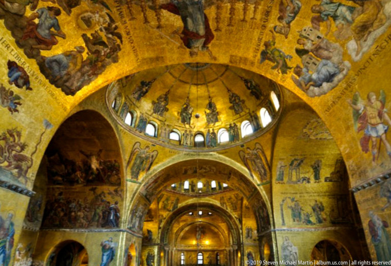 Golden mosaic-covered domes and arches inside St. Mark's Basilica, with small windows circling the central dome above the nave.