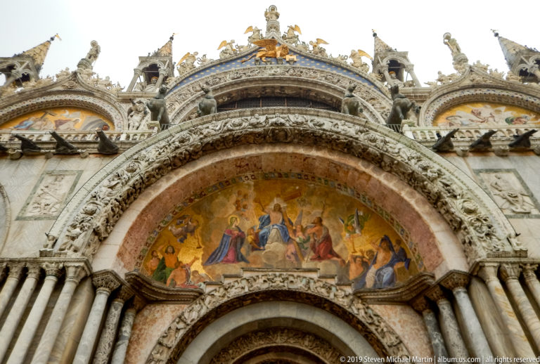 Gold mosaic lunette with central seated figure and attendants above carved arches and marble columns.