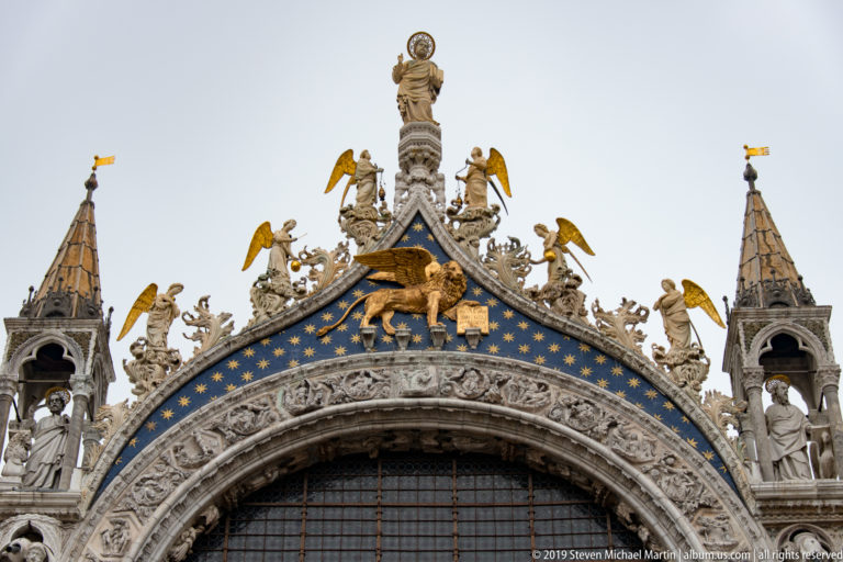 Central upper gable of St. Mark’s Basilica with winged lion, saints, gilded angels, pinnacles, and carved cresting.