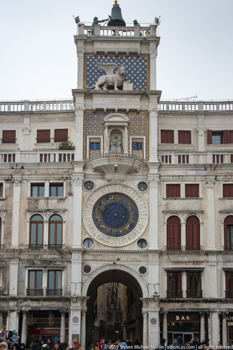 Full St. Mark’s Clock Tower façade with passage arch, astronomical clock, upper panels, and rooftop bell.