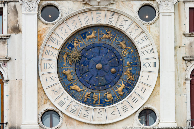 Blue astronomical clock with gilded zodiac signs and Roman numeral ring on St. Mark’s Clock Tower.