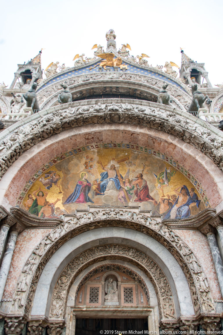 Gold mosaic lunette above concentric carved stone arches and the upper portion of a St. Mark’s Basilica portal.