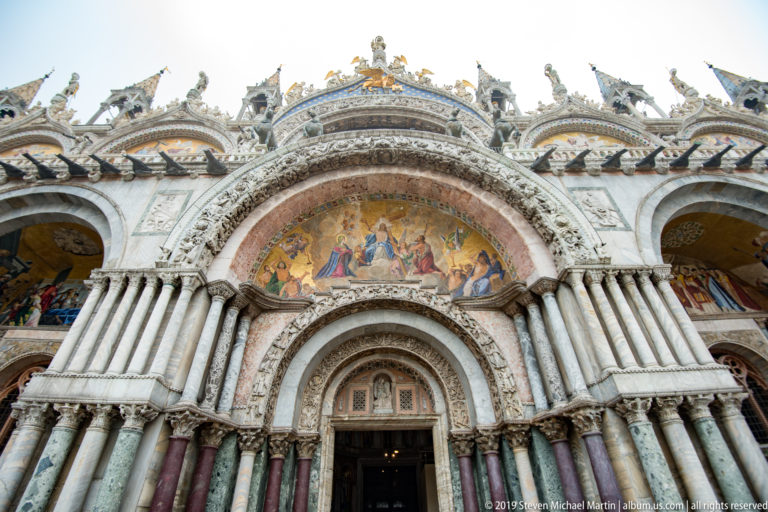 Central portal of St. Mark’s Basilica with carved arches, clustered marble columns, mosaic lunette, and ornate roofline.