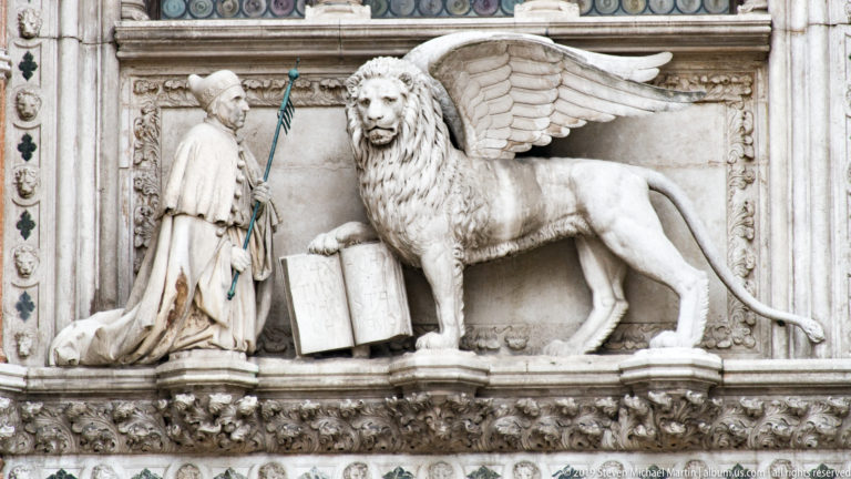 Marble relief of the winged Lion of St. Mark beside a kneeling robed figure and open book.