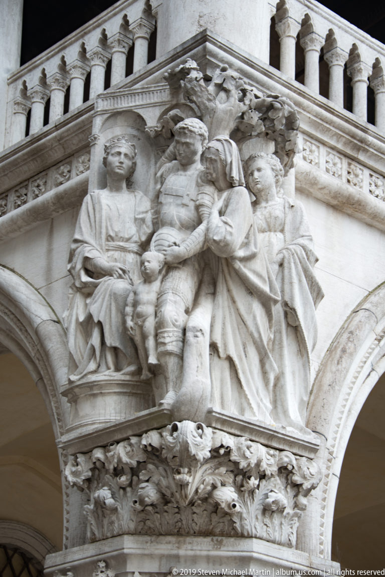 Carved marble group with seated central figure and attendants projecting above an arcade and below a balustrade.
