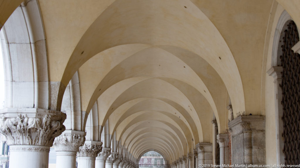 Long covered arcade with repeating pale vaults and carved stone columns receding into the distance.