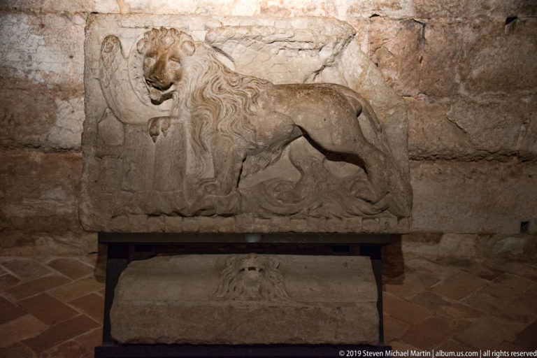 Weathered rectangular stone relief of a lion displayed above a smaller carved fragment.