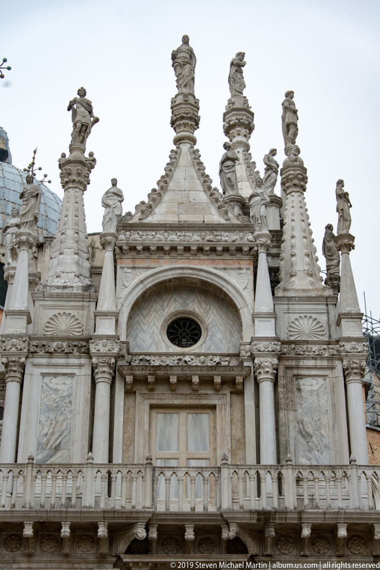 Pale Gothic gable with pinnacles, finials, circular opening, and relief panels in the courtyard of the Doge’s Palace.