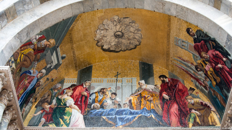 Gold-ground arched mosaic showing figures gathered around a reclining person, beneath a large central floral boss.