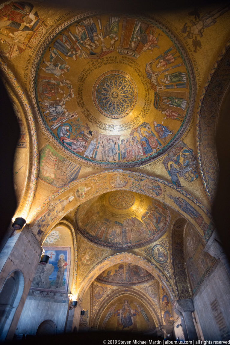 Several gold mosaic domes receding through St. Mark’s Basilica, with figures and scenes illuminated against darker arches.