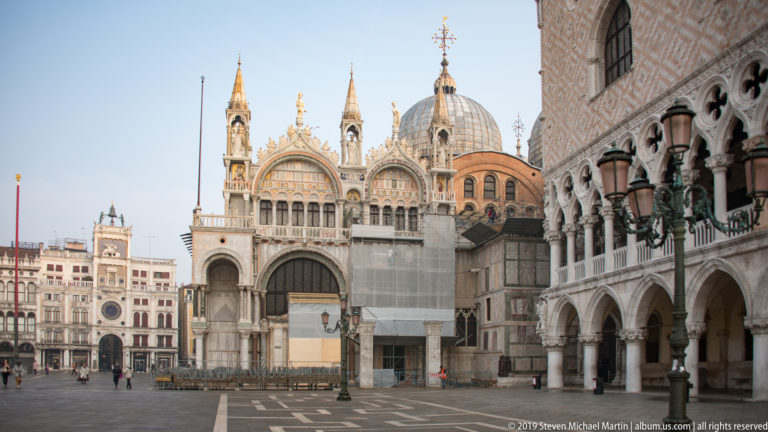 St. Mark’s Basilica with domes and arched façade beside the arcaded Doge’s Palace, with conservation screening at right.