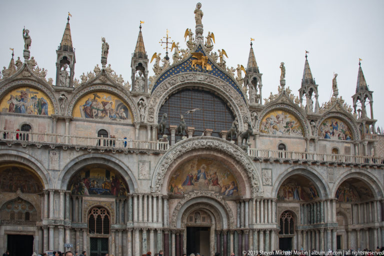 Frontal view of St. Mark’s Basilica with five portal bays, mosaics, central window, columns, pinnacles, and statues.