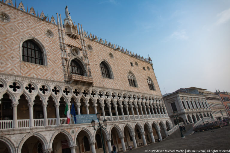 Oblique exterior view of the Doge’s Palace with long Gothic arcades, patterned upper wall, and ornate roofline.