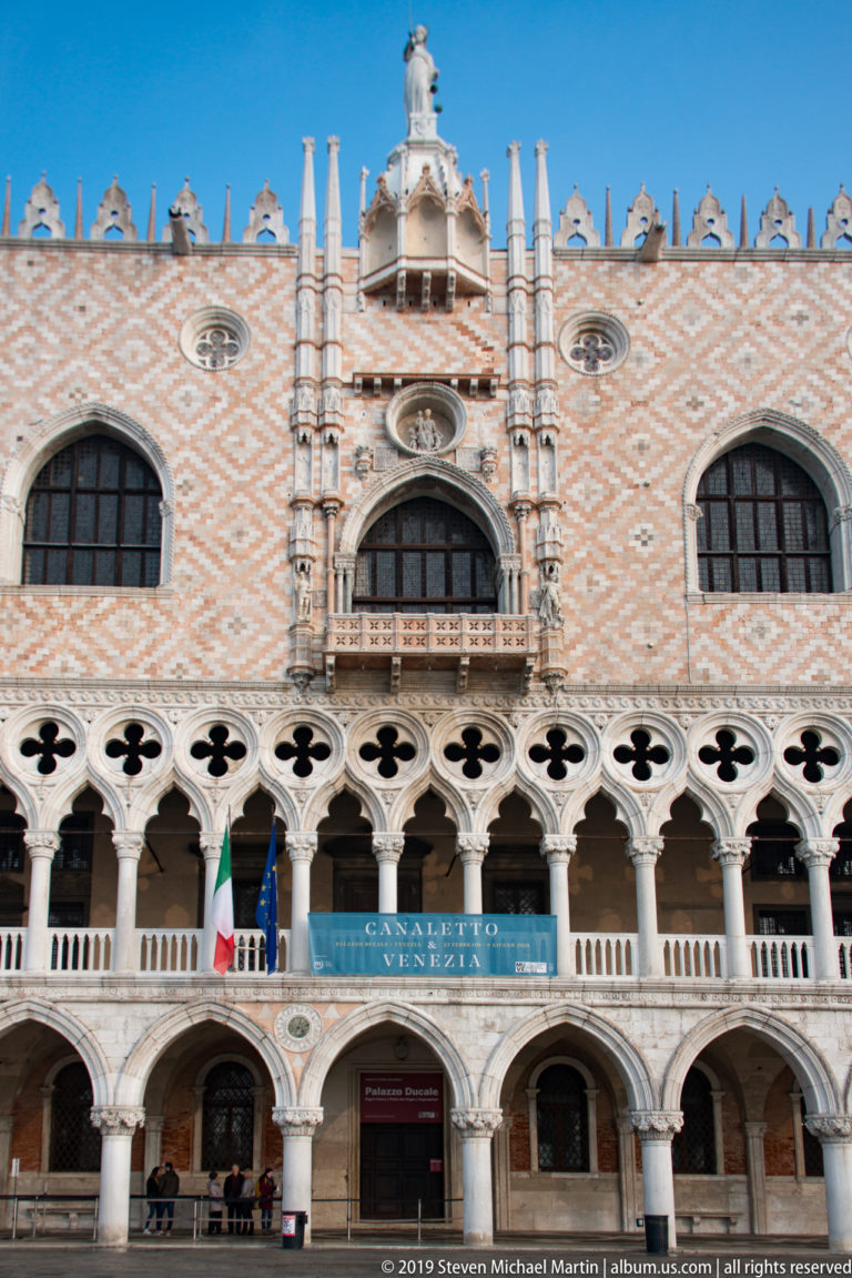 Doge’s Palace façade with pink diamond-patterned masonry, arched windows, quatrefoil openings, and two levels of pale Gothic arcades.