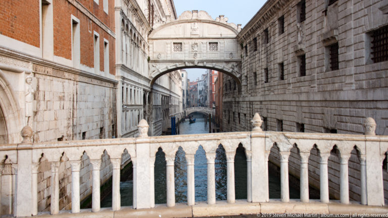 Centered Bridge of Sighs above the Rio di Palazzo, framed by a pale Gothic balustrade and tall stone walls.