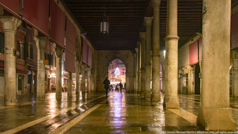 Colonnaded passage seen from the opposite direction under nighttime illumination in Venice.