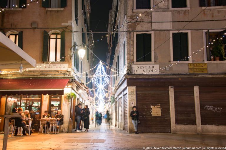 Street café beneath holiday lights under nighttime illumination in Venice.