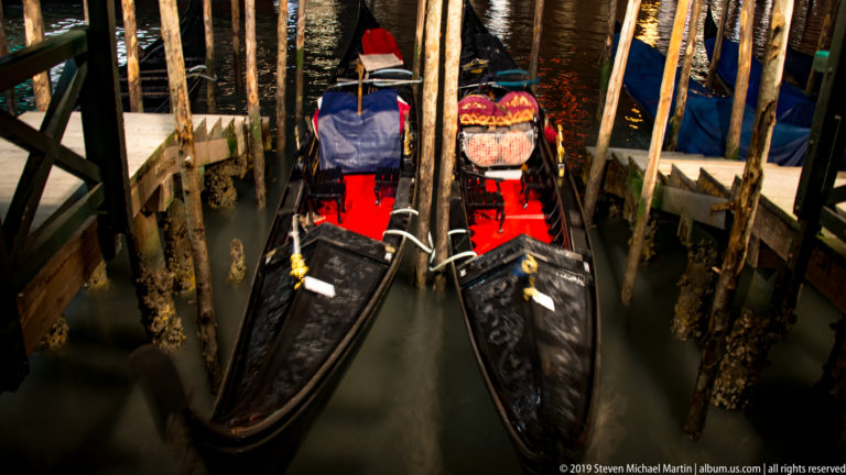 Two gondolas seen from above at their moorings under nighttime illumination in Venice.