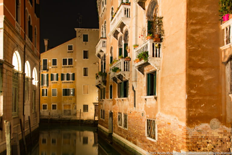 Quiet narrow canal between residential façades under nighttime illumination in Venice.