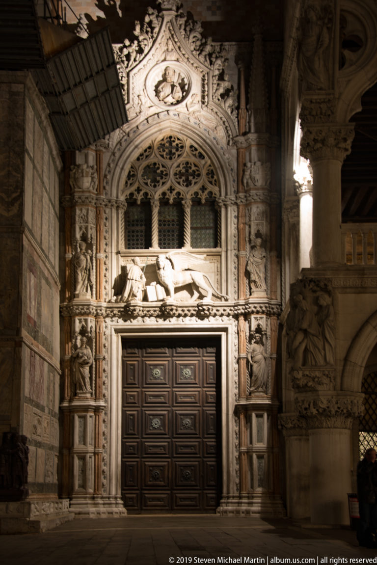 Floodlit Gothic Porta della Carta with paneled door, tracery, niches, and carved stone figures at the Doge's Palace.