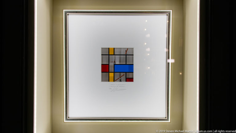 Framed geometric abstract print with black grid lines and red, yellow, and blue rectangles displayed behind glass.