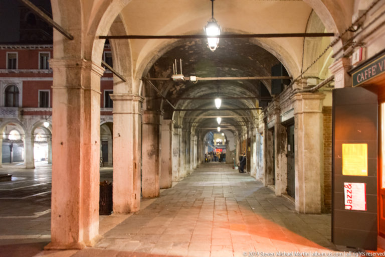 Stone arcaded passageway at night under nighttime illumination in Venice.