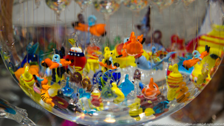 Close-up of colorful miniature glass animal figurines, including ducks and fish, clustered inside a clear display bowl.