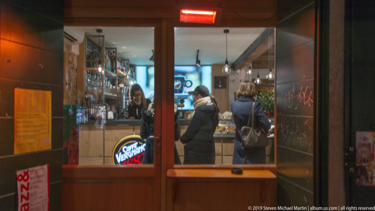 Small food-and-drink shop viewed through its entrance under nighttime illumination in Venice.