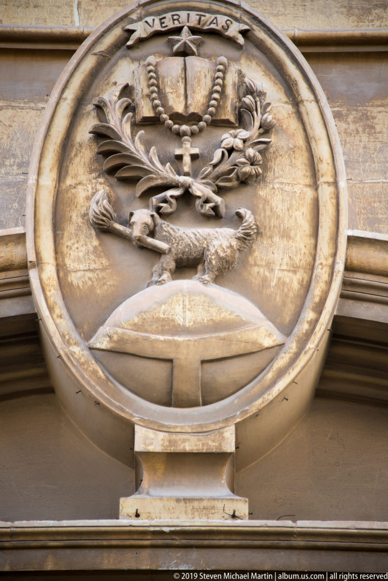 Circular stone medallion inscribed VERITAS with crossed symbolic objects, foliage, and sculptural ornament above an entrance.