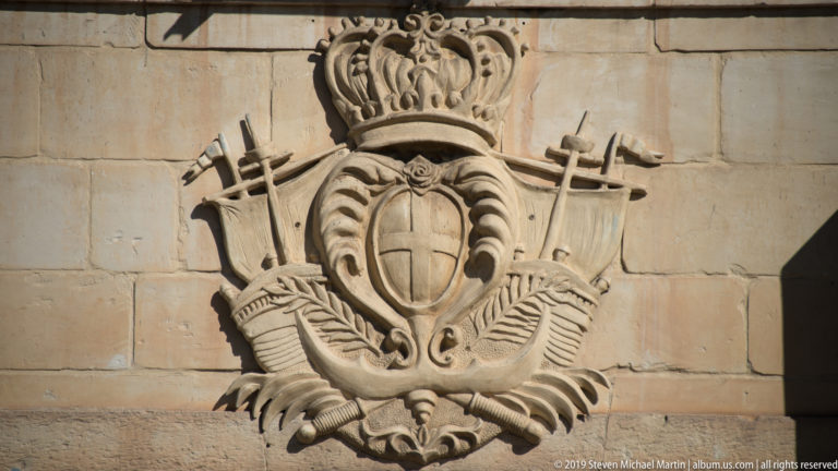 Limestone relief of a crowned shield surrounded by crossed weapons, standards, armor, and other military emblems.