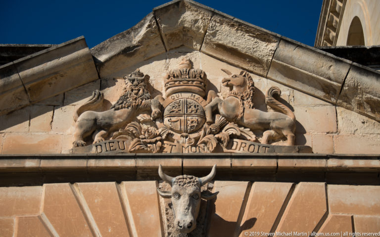 Carved crowned royal arms with lion, unicorn, shield, and the motto Dieu et mon droit in a limestone pediment.