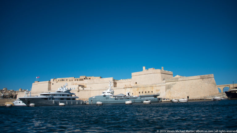 Broad pale limestone bastions of Fort St Angelo rising above Grand Harbour, with yachts and small boats along the waterline.
