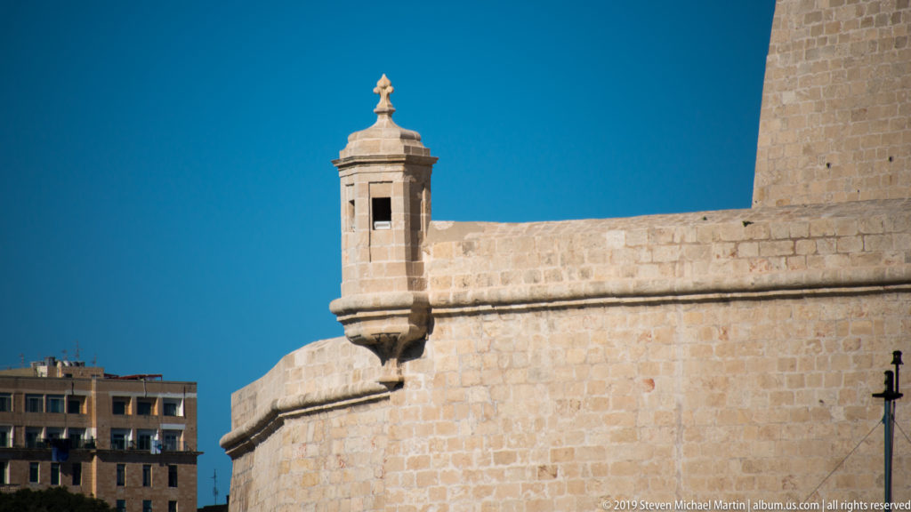 Close view of a narrow projecting stone sentry box with small openings and carved finial on a limestone bastion corner.