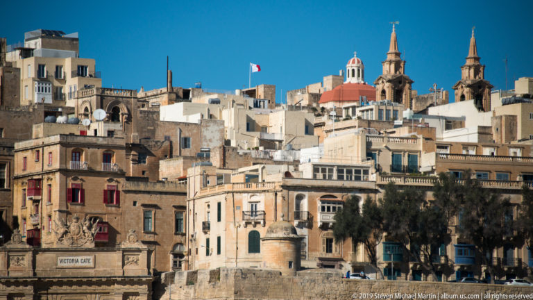 Vittoriosa waterfront with layered limestone buildings, church domes and bell towers rising above the stone quay.