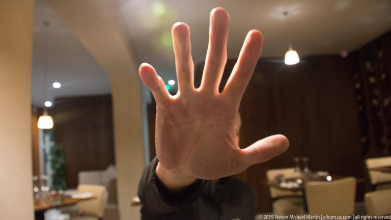 Open hand held close to the camera inside a warmly lit restaurant, with tables and chairs blurred in the background.