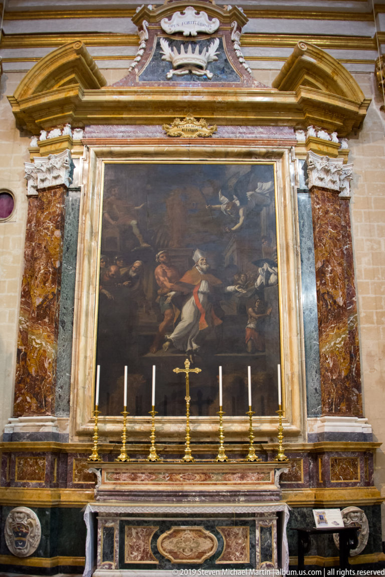 Large dark religious painting in a marble and gilded altar frame above candlesticks and a central crucifix.